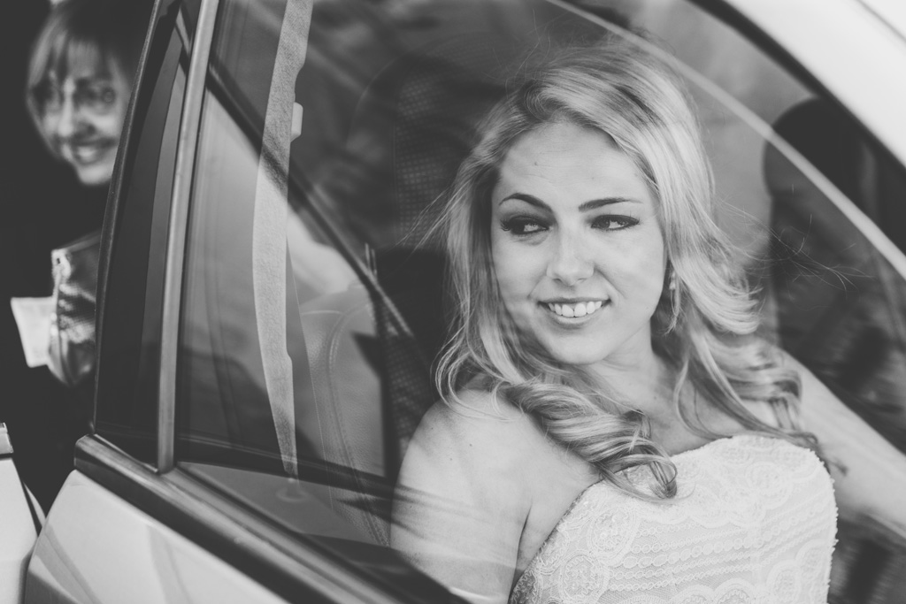 La sposa sorride raggiante dalla macchina con lo sguardo in direzione della Basilica