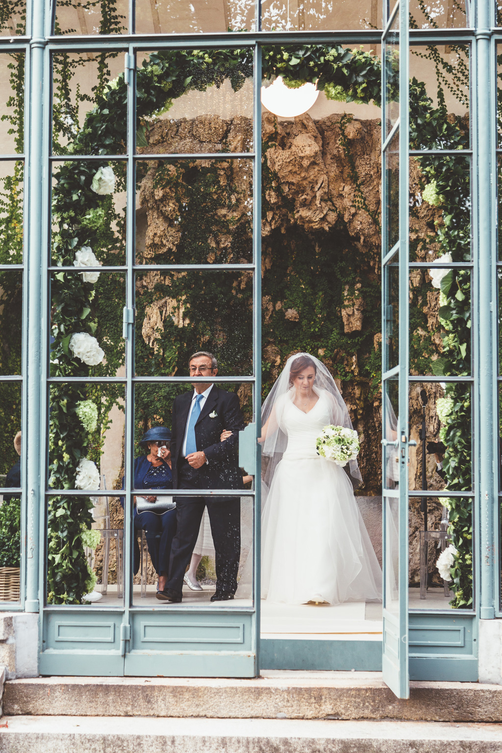 Il padre e la figlia Daniela superano la porta a vetro per raggiungere lo sposo in una foto di Della Savia fotografo presso Milano