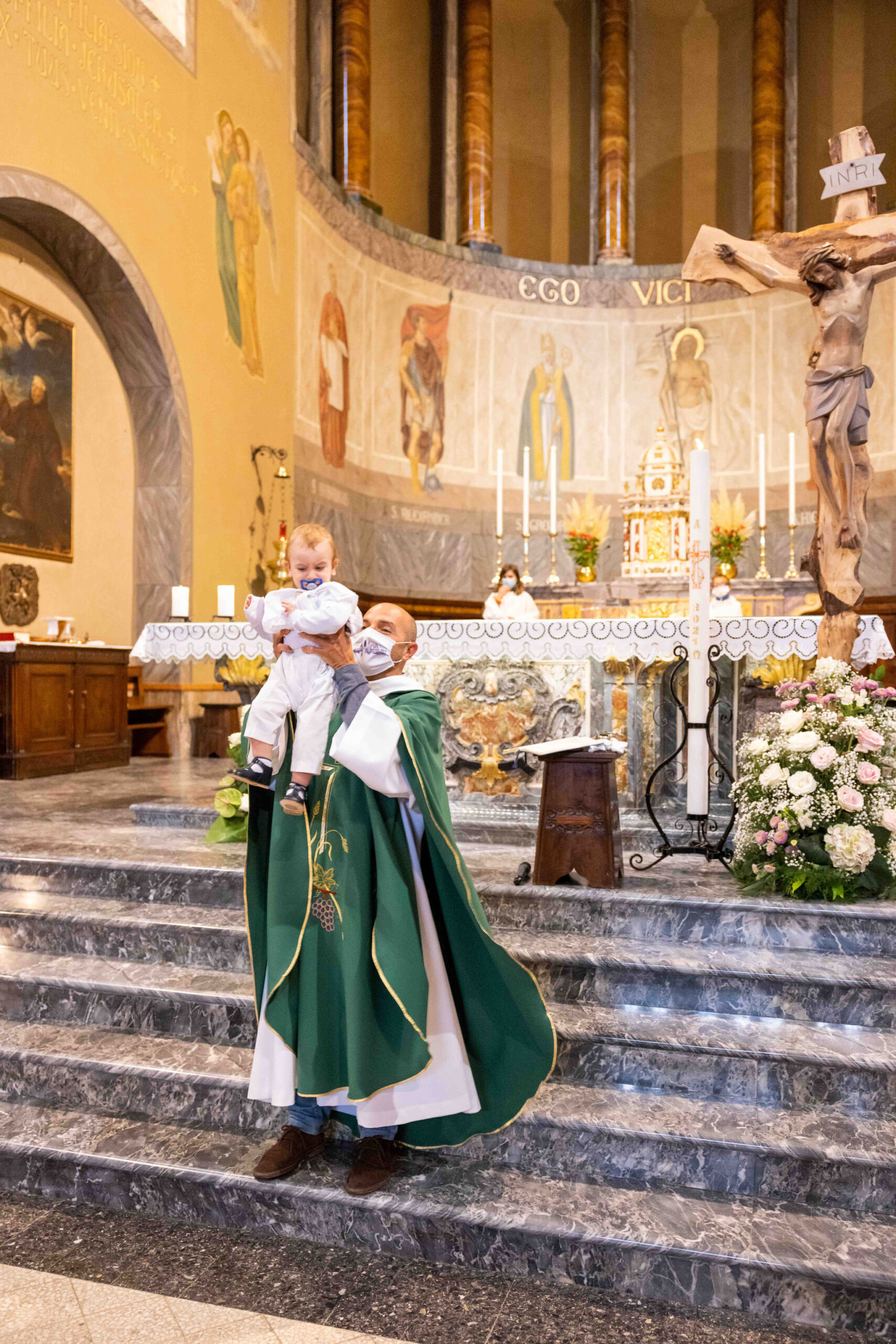 Bambino con sacerdote durante il battesimo nella parrocchia di comenduno